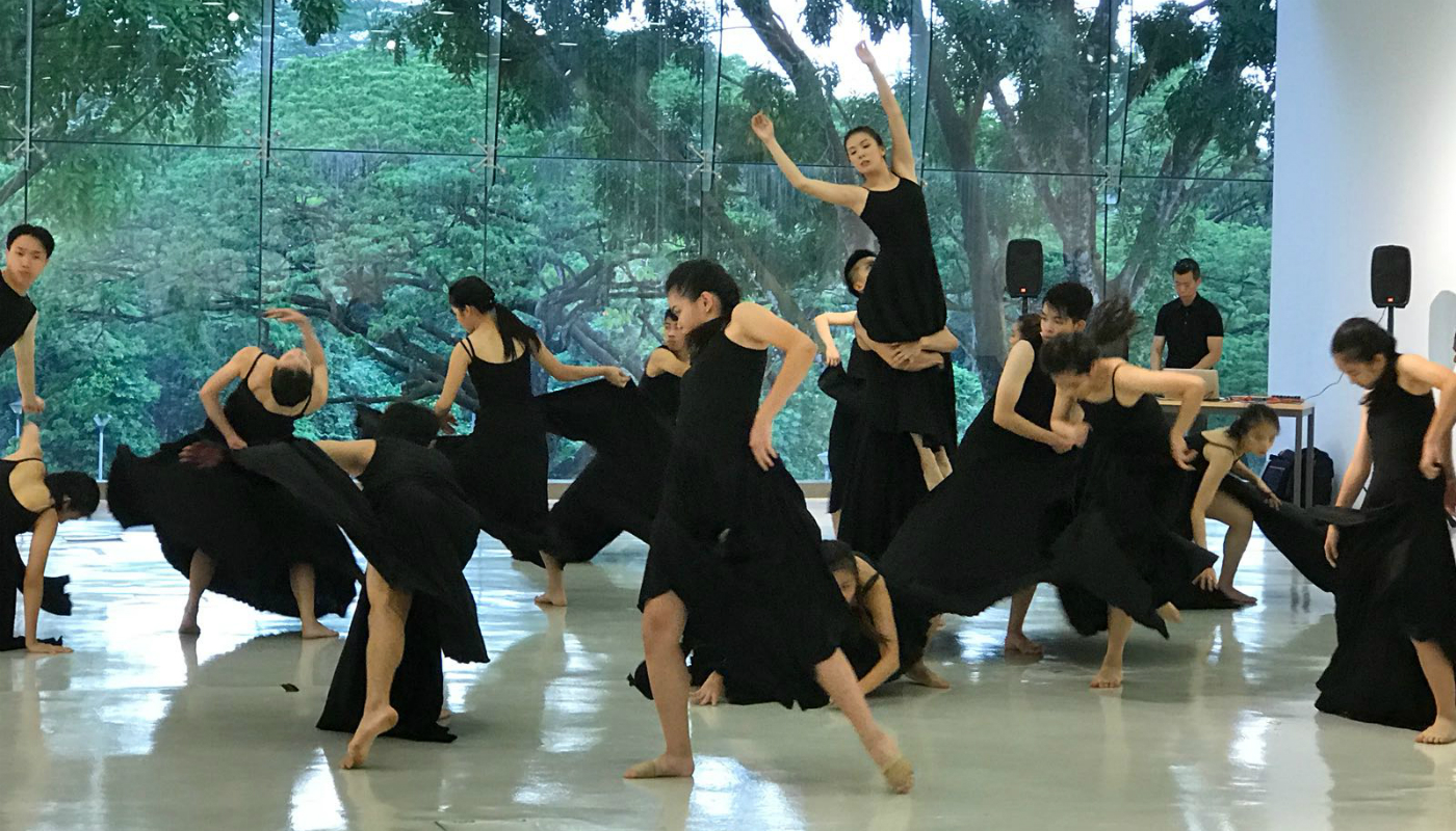 A group of male and female dancers rehearsing in a studio in front of greenery