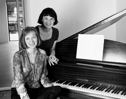 Musical Theatre writing duo Caroline Wigmore and Jen Green posing by a grand piano with lid open
