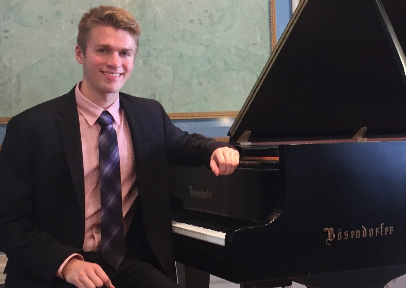 Garrett Snedeker wearing a jacket and tie, seated, and resting one arm on top of a grand piano.