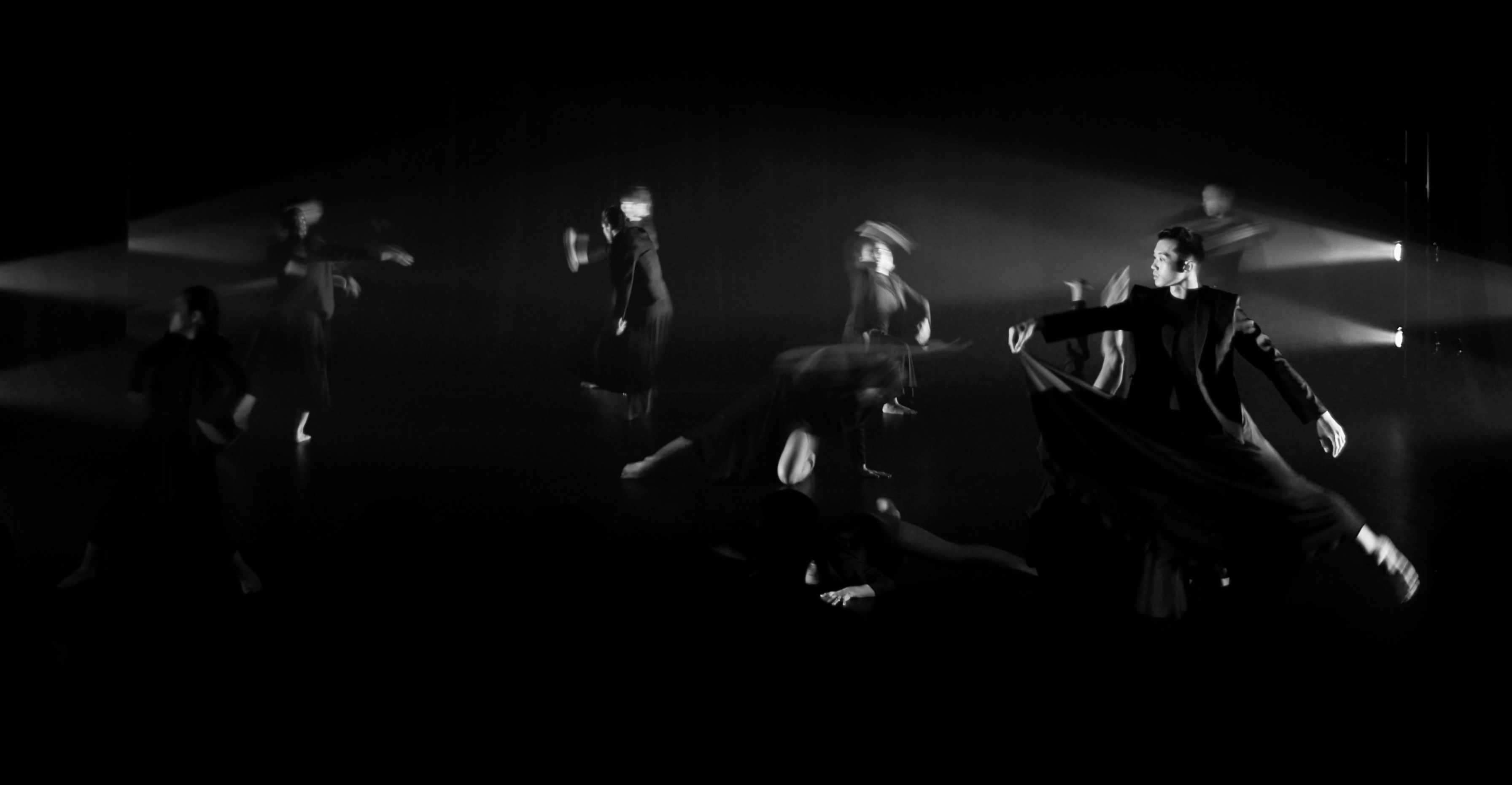 Black and white blurred shot of dancers in motion on stage with side lighting