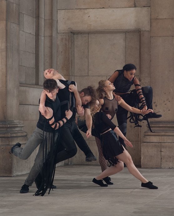 Six dancers all holding on to each other in motion