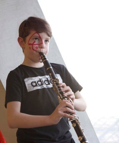 Image of a young musician playing the clarinet, whilst wearing red face paint of a triangle around his eye