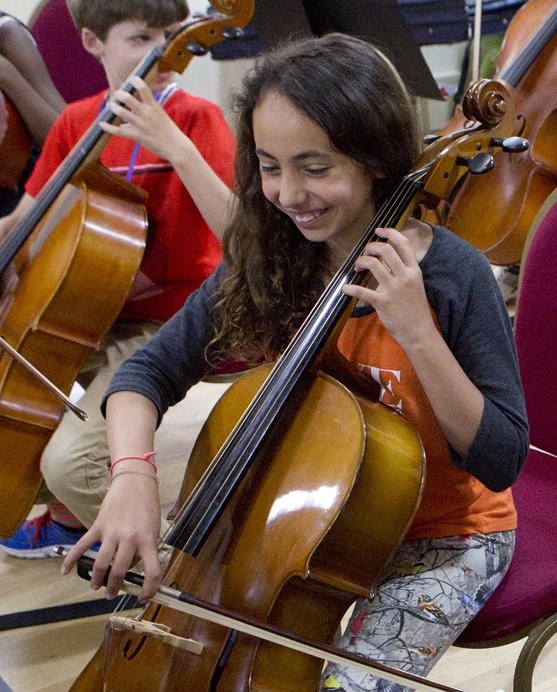 A young person smiling playing the cello