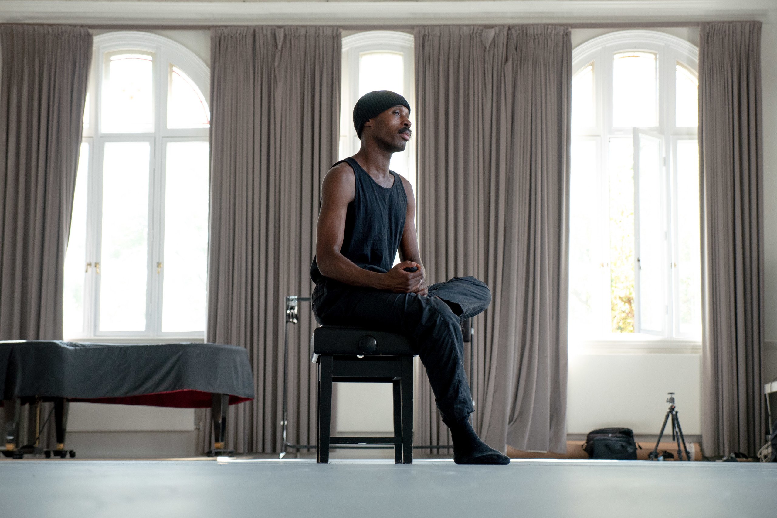 Choreographer Theo TJ Lowe sits on a piano stool in the centre of a studio space
