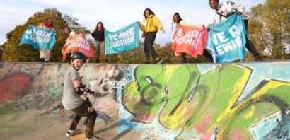 Skateboarders in graffitied outdoor skate park with 'We Are Lewisham' signs