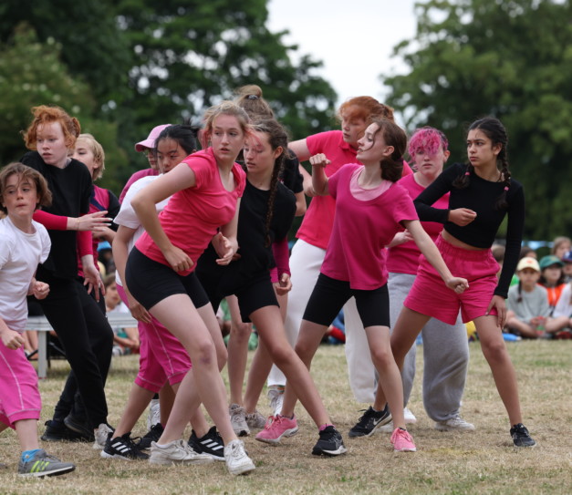 Group of young dancers in bright pink and black t-shirts and shorts perform in front of children