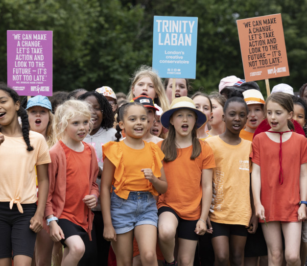Group of young performers in bright orange t-shirts, singing and holding protest placards