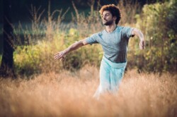 Nathaniel Parchment dancing in a field of long grass. He is wearing a grey top and light blue trousers.
