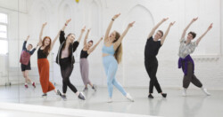 Seven Trinity Laban students practicing in a white dance studio.