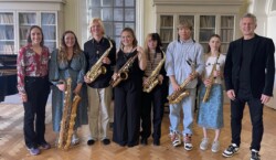 Participants of the Trinity Laban Saxophone Competition stand in a row facing the camera.