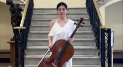Xiaodi Zhao, the new recipient of the Bagri Foundation Scholarship stands holding her cello in front of a large staircase.